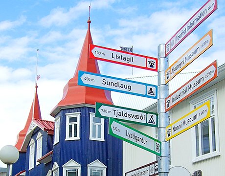 Colorful signpost pointing to local attractions in Akureyri, Iceland, with charming red-roofed buildings nearby | MSC Cruises