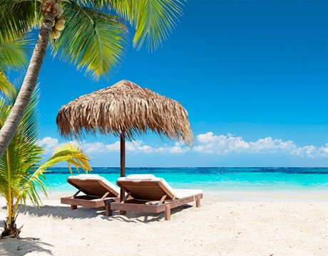 Two lounge chairs under a thatched umbrella on a tropical beach with turquoise water | MSC Cruises