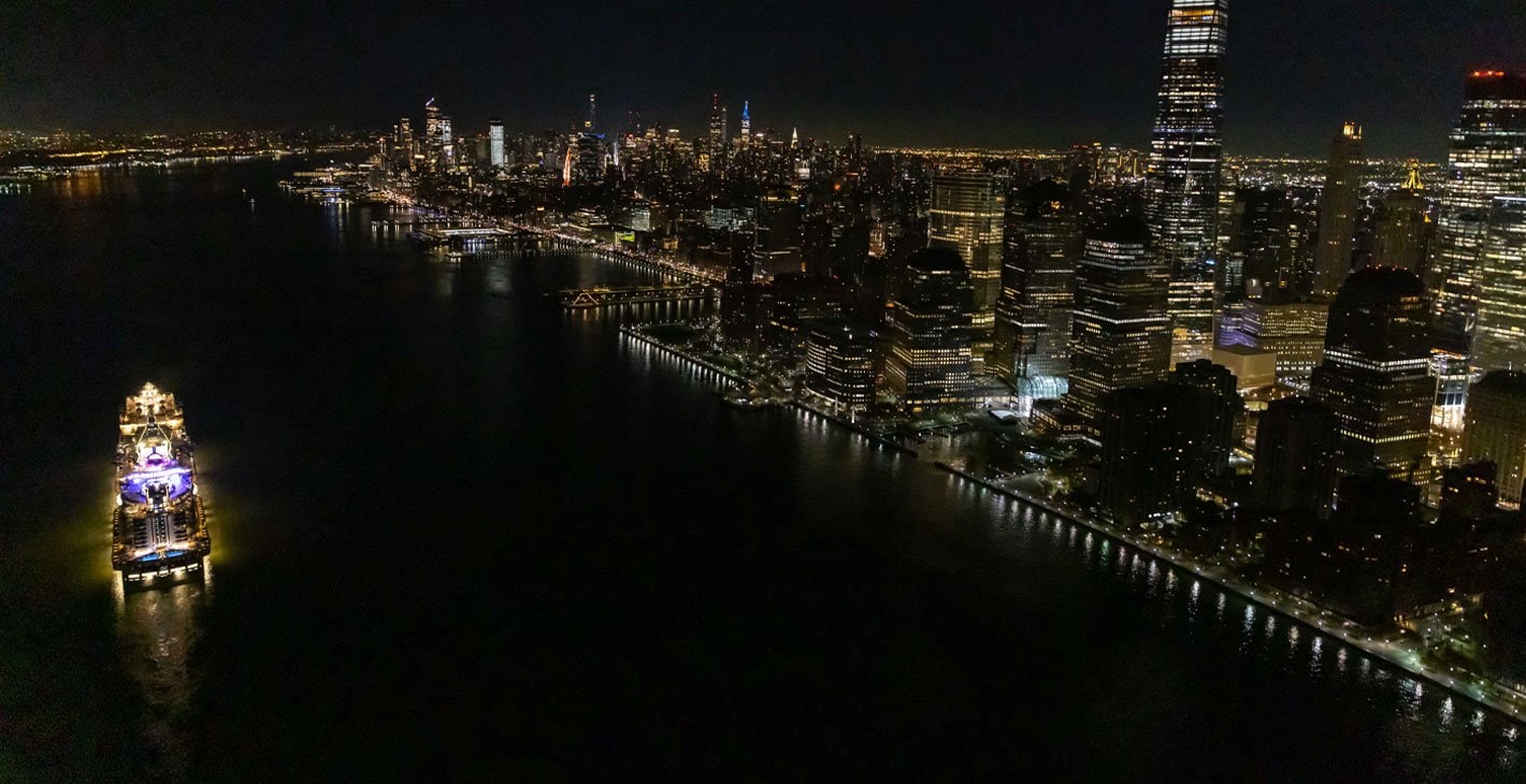 An illuminated MSC cruise ship sailing near New York City's skyline at night | MSC Cruises