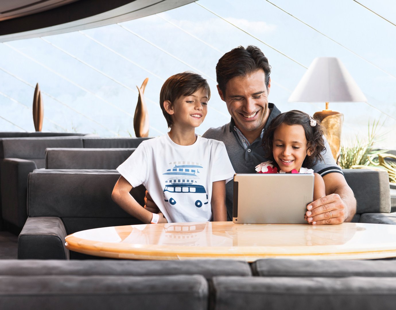 A family enjoying leisure time with a tablet in a modern cruise lounge | MSC Cruises A family enjoying leisure time with a tablet in a modern cruise lounge | MSC Cruises