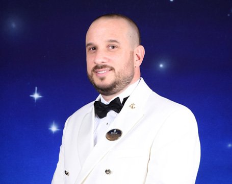 A crew member in a white formal uniform against a starry background | MSC Cruises